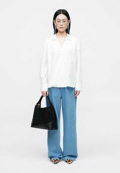 Witte button-up shirt, losse blauwe denim broek, zwarte suède schoudertas en beige schoenen met een luipaardprint. Duidelijke brillen en hangende oorbellen.