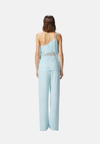 Camisola di raso azzurro chiaro con dettagli in pizzo, abbinata a pantaloni larghi coordinati. Presenta un design con una sola spallina.