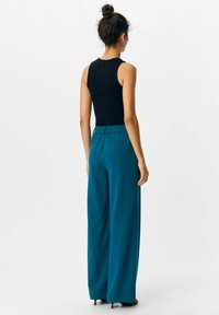 Svart ärmlös topp och teal vida byxor med elastisk midja, som visar ett mjukt tyg och en avslappnad passform från bakifrån.