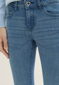 Jeans de mezclilla azul con una textura suave, corte ajustado y un diseño clásico de cinco bolsillos. Presenta un botón plateado y un desgastado sutil.