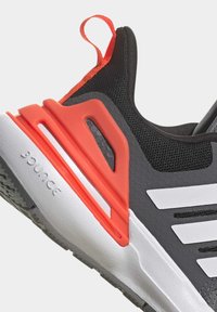 Zapatilla deportiva negra con parte superior de tejido texturizado, detalles en naranja y rayas blancas. Cuenta con una suela acolchada y una pestaña en el talón.