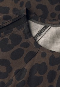 Tessuto marrone con motivo a stampa leopardata nera. Primo piano di un collo con dettagli della cucitura ben visibili e una texture liscia. Nessun'altra caratteristica.