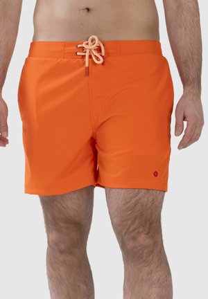 Man wearing bright orange swim shorts with front lace-up detail and small red logo on left leg, standing against plain background.