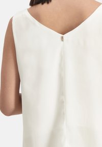 Witte mouwloze blouse met een V-vormige rug, voorzien van een kleine gouden accentknop en gemaakt van gladde, lichtgewicht stof.