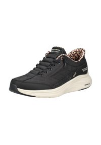 Μαύρα μοκασίνια Skechers slip-on με επάνω μέρος με καπιτονέ ραφή, φόδρα με σχέδιο λεοπάρδαλης, λευκή καμπυλωτή σόλα και μαύρα κορδόνια.