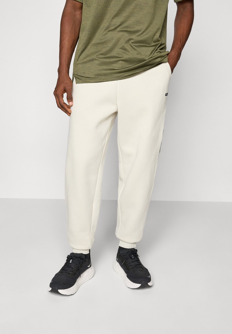 Cremefarvede fleece joggers med elastiske manchetter, parret med en mørkegrøn top. Sorte sportsko supplerer outfittet.
