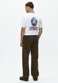 Witte katoenen t-shirt met een ronde grafische print in blauw en bruin, gecombineerd met een bruine corduroy broek met een rechte pijp en achterzakken.