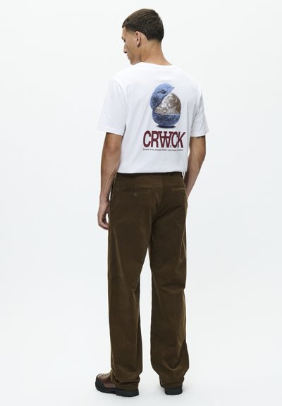 T-shirt en coton blanc avec un graphique circulaire bleu et marron, associé à un pantalon en velours côtelé marron avec une coupe droite et des poches arrière.