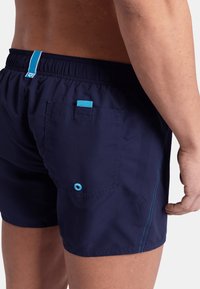 Pantaloni da bagno blu navy con vita elasticizzata, cuciture blu a contrasto e tasca sul retro con un bottone blu decorativo.