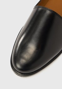 Μαύρο δερμάτινο παπούτσι με λείο, γυαλιστερό φινίρισμα, στρογγυλεμένη μύτη και ελάχιστες ραφές κατά μήκος της ραφής. Η σόλα είναι επίπεδη και ελαφ ρώς υφή.