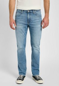 Ljust blå denimjeans med regular fit, femfickdesign och subtila blekningar. Matchas med svarta och vita high-top sneakers.