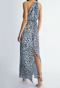 Maxikleid aus lichtblauem Stoff mit schwarzem Leopardenmuster, Halterneck, gerafftem Rücken und Schlitz bis zum Oberschenkel. Kombiniert mit weißen High Heels.