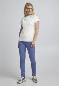 Hvid kortærmet top med rund halsudskæring og plisse-detalje, sat sammen med slim-fit lyseblå bukser og beige træningssko.