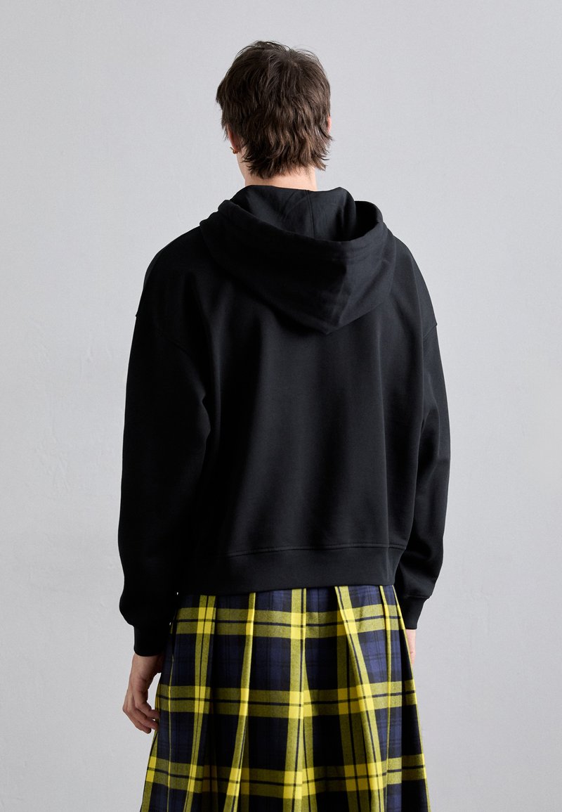 Felpa cropped nera con un ampio cappuccio, abbinata a una gonna kilt a quadri gialli e blu navy. Presenta un design semplice e senza fronzoli.