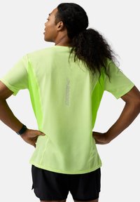 Neono žalias lengvas sportinis marškinėlis su tekstūruotu raštu, trumpomis rankovėmis ir atspindinčiu prekės ženklu ant nugaros. Derinama su juodomis šortais.