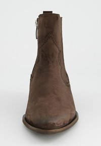 Bota de tacón bajo de ante marrón con punta redonda, costuras decorativas, cremallera lateral y suela de goma plana. Textura suave con detalles mínimos.