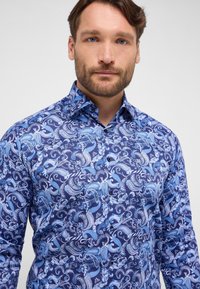 Herenoverhemd in een blauw paisleypatroon, met tinten lichtblauw en wit. Gemaakt van stof met een glad oppervlak en een knoopsluiting.