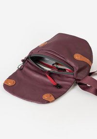 Borsa verticale bordeaux in materiale morbido, con dettagli in pelle color cuoio, un pattino frontale con bottoni a pressione e una tasca interna con zip.