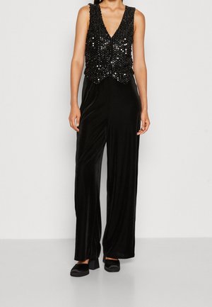 Haut sans manches noir à paillettes avec col en V, associé à un pantalon large taille haute en velours noir et à des chaussures noires à talons blocs.