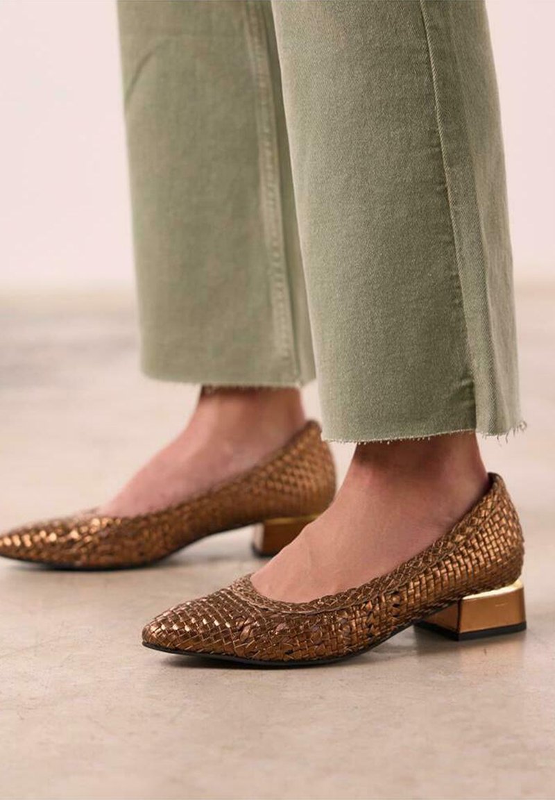 Chaussures en cuir tressé bronze avec un talon carré, présentant un bout pointu et une tige texturée, associées à un pantalon court vert clair.
