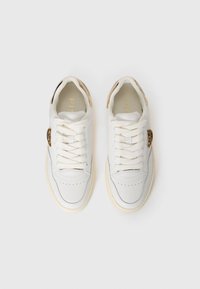 Una coppia di sneakers bianche basse con spesse stringhe bianche, suole beige e un accento metallico dorato sul lato esterno di ciascun scarponcino.