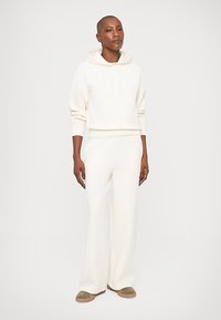 Cream hooded sweatshirt with ribbed cuffs, paired with cream wide-leg pants. Soft fabric, relaxed fit, minimal stitching details.