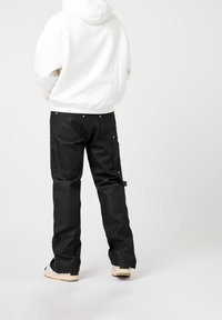 Un pantalon cargo noir doté de multiples poches et de détails en métal argenté, associé à un sweat à capuche blanc pour un contraste saisissant.