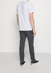 Bílá krátká košile s černými puntíky, v kombinaci s tmavě šedými slim-fit kalhotami a černými teniskami. Zadní pohled.