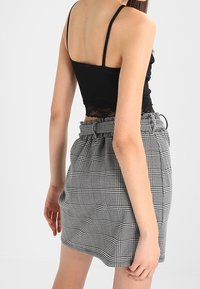 Top nero senza maniche con pizzo, abbinato a una gonna a quadretti con cintura e vita elastica. La gonna ha una forma strutturata.