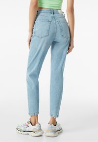 Ljusblå högmidjade jeans med raka ben, fem fickor och subtila blekningar. Matchas med kraftiga grå sneakers med färgglada detaljer.