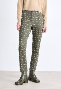 Olijfgroene broeken met een herhaald tijgerpatroon in beige. Heeft zijbanen, een gladde textuur en een slim fit ontwerp. Gecombineerd met groene haklaarsjes.