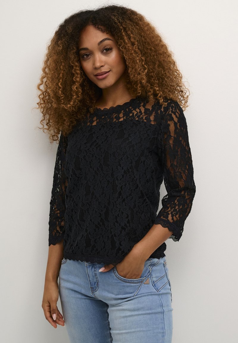 Black lace top with three-quarter sleeves, scalloped neckline, intricate floral pattern, worn over light blue jeans.