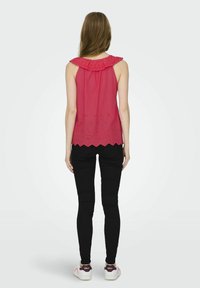 Top sin mangas de color rosa con un escote con volantes, detalles de ojales en el dobladillo, combinado con jeans ajustados negros y zapatillas blancas informales.