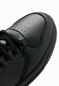 Baskets en cuir noir présentant une texture lisse, un embout perforé et des lacets noirs ; forme arrondie avec des coutures renforcées et une semelle en caoutchouc.