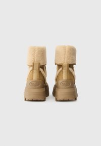 Botas amarelas em pele sintética com um colarinho alto e peludo e solas grossas em bege. Apresentam um logo no calcanhar e uma sola texturizada para maior aderência.