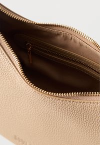 Μπεζ υφασμάτινο δερμάτινο σακουλάκι με χρυσό φερμουάρ, ανοιχτό για να φαίνεται το επενδεδυμένο εσωτερικό και η μικρή εσωτερική τσεπούλα με φερμουάρ.