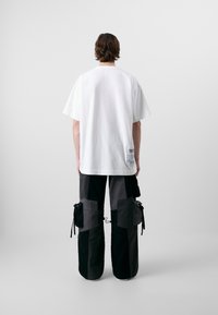 Witte katoenen t-shirt met korte mouwen en een label op de onderrug, gecombineerd met baggy zwarte en grijze cargobroek met zakken en trekkoorden.