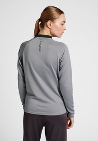 Maglietta atletica grigia a maniche lunghe con un motivo testurizzato, dotata di un colletto scuro e dettagli dell'etichetta sul retro, abbinata a pantaloni scuri.