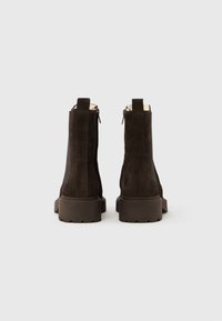 Καφέ καστόρινες μπότες αστραγάλου με υφή, που διαθέτουν ταινία έλξης και ανθεκτική καουτσούκ σόλα για σταθερότητα. Πλευρικά φερμουάρ για εύκολη φορεσιά.