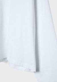 Primo piano di una T-shirt bianca in cotone a maniche corte che mostra la trama del tessuto e le cuciture dell'orlo su uno sfondo chiaro.