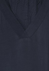 Top de cuello en V de color marino, confeccionado con tejido ligero. Presenta una textura suave, ligeramente arrugada, con bordes y costuras limpias.