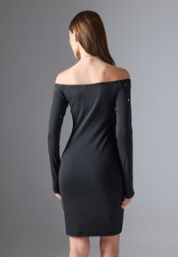 Schwarzes, schulterfreies, geripptes Kleid mit langen Ärmeln. Verziert mit metallischen Nieten entlang der Ärmel, figurbetonte Silhouette, knielange Länge.