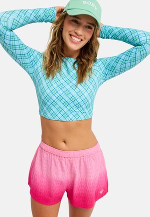 Lyseblå crop-top med lange ærmer og ternet mønster, kombineret med pink ombre-shorts med tekstureret finish og elastik i taljen.