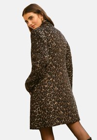 Palton cu imprimeu leopard, cu un finisaj moale și texturat, având o siluetă lungă și un guler tip șal. Accentuate cu buzunare laterale mici.