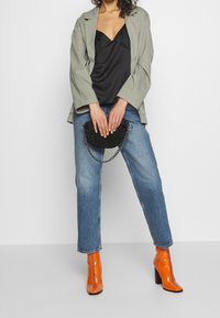 Grön rutiga oversized kavaj, svart satin cami, ljusblå raka jeans och oranga lackläder ankelstövlar. Svart pärlhandväska med kedja.