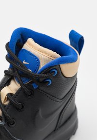 Czarne sneakersy z teksturowanego materiału, niebieskie akcenty na kołnierzu i oczkach, oraz beżowy wyściełany język. Posiadają czarne sznurowadła.