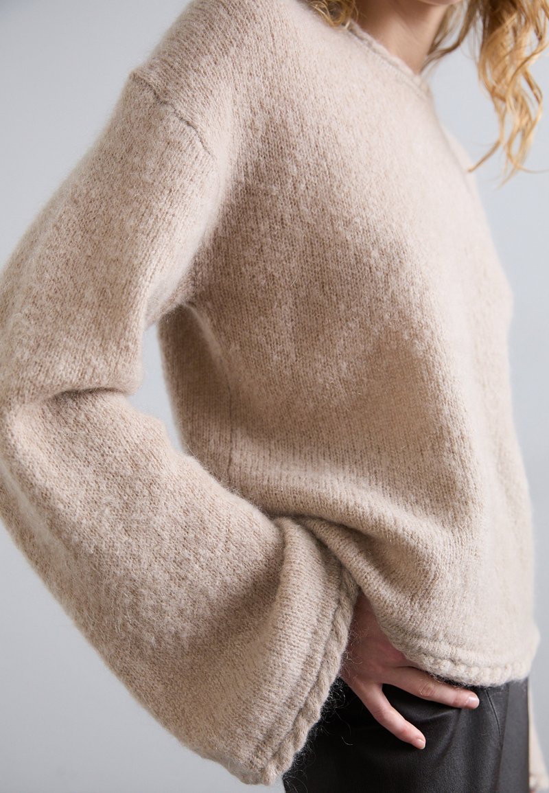 Maglione beige lavorato a maglia con una vestibilità ampia, maniche larghe e orli a coste. Il tessuto morbido e testurizzato offre un aspetto accogliente.