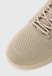 Μπεζ αθλητικό παπούτσι με υφασμάτινο επάνω μέρος με υφή, ομαλή μύτη και εν ισχυμένη περιοχή για τα κορδόνια, με στενές τρύπες για διαπνοή.