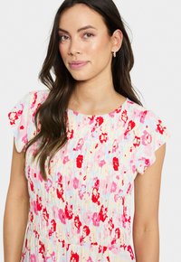 Robe fleurie avec des manches courtes et volantes. Présente un fond pastel avec des fleurs rouges et roses éclatantes. Taille élastique, tissu léger.