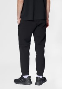 Schwarze, taillierte Jogginghosen mit Reißverschlusstaschen, gerippten Bündchen und einer glatten Textur, kombiniert mit schwarzen Sportschuhen.